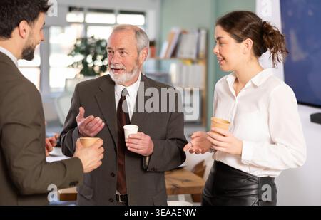 Pause café - les hommes et les jeunes femmes boivent du café et discutent animés les uns avec les autres dans un bureau moderne Banque D'Images