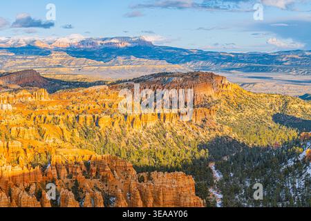 vue panoramique sur Bryce Canyon hoodoos baignés dans la lumière dorée du matin avec des montagnes enneigées et des forêts de pins au loin. Banque D'Images