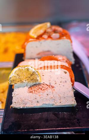 Un gâteau aux fruits se trouve sur une assiette sombre dans un présentoir de desserts. Il a des tranches d'orange sur le dessus et est fait avec des morceaux de fruits. Ce gâteau se trouve dans une boulangerie d. Banque D'Images