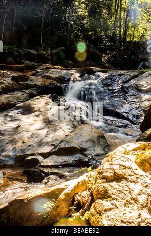 Une petite cascade sereine coule sur des rochers sombres et étincelants dans un flux continu et doux, capturant la beauté pure et brute de la nature en mouvement dans Bra Banque D'Images