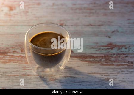 Vue latérale du café sale en couches dans le verre à double paroi sur la table en bois rustique. Lumière du soleil d'heure dorée chaude du matin avec espace de copie. Banque D'Images