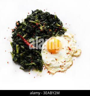 Plat sain avec un oeuf frit et un côté de légumes verts feuillus sautés piment sur fond blanc. Concept de cuisine méditerranéenne. Vue de dessus. Banque D'Images