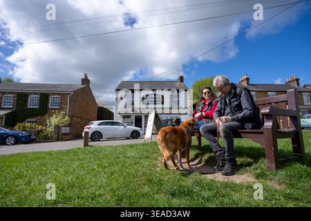 Les marcheurs mâles et femelles se reposent sur le banc avec leur chien devant la boutique du village à Sarratt, Herts Banque D'Images