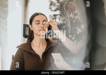 Maquilleuse appliquant le fard à paupières à une femme détendue dans un centre de beauté lors d'une séance de maquillage professionnel Banque D'Images