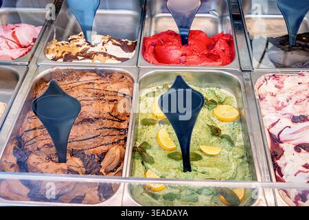 Cuillères tentant diverses saveurs de gelato, y compris le chocolat, la menthe, la fraise, et d'autres desserts sucrés dans une boutique Banque D'Images