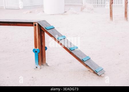 Parc pour chiens doté d'une rampe d'agilité en bois avec des marches bleues sur le sable, fournissant de l'équipement pour l'entraînement et l'exercice des animaux de compagnie Banque D'Images