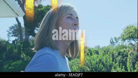 Regarder la femme tourner dans le jardin, bleu-dessus, montrant le toit, arbustes, fusée verticale-orange, boucle d'oreille Banque D'Images