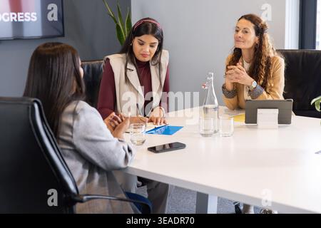 Diverses collègues féminines se réunissant à la table de conférence en tenue d'affaires, écrivant sur le bloc-notes bleu Banque D'Images