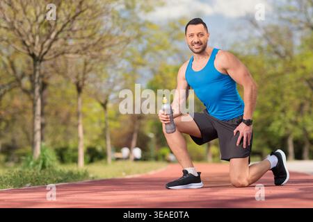 Homme agenouillé sur une piste de course et tenant une bouteille d'eau Banque D'Images
