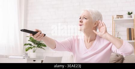 Femme âgée la hausse du volume d'un téléviseur avec télécommande Banque D'Images