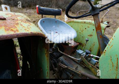 Siège de tracteur et volant rouillés avec corps et commandes métalliques usés sur une vieille machine agricole extérieure. Banque D'Images