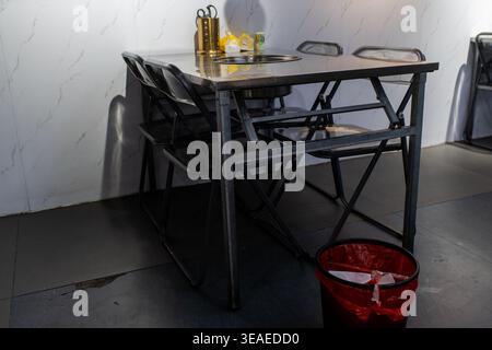 Table et chaises pliables en métal dans un coin restaurant minimaliste avec poubelle rouge et marbre Banque D'Images