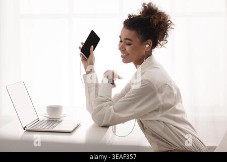 Jeune femme aime la musique tout en travaillant sur ordinateur portable dans l'espace de travail moderne Banque D'Images