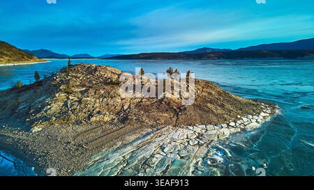 Lac gelé aérien affleurement rocheux et arbres conifères en paysage hivernal Banque D'Images