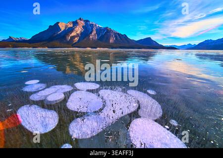 Bulles de méthane gelées sous la glace avec des reflets de montagne enneigés Winter Lake Banque D'Images