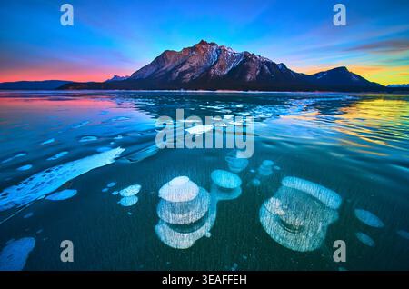 Bulles de méthane gelées et reflets de montagne sur Winter Lake au coucher du soleil Banque D'Images