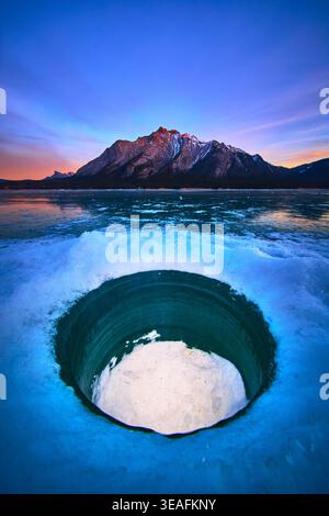 Trou de pêche sur glace sur le lac gelé avec montagne et soleil d'hiver vibrant Banque D'Images