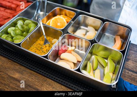 Variété de fruits tranchés colorés, y compris la pastèque, l'orange, le raisin, le fruit de la passion, le melon et la garniture de fruits de cantaloup dans un récipient en métal au bar Banque D'Images