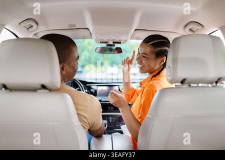 Heureux jeune couple noir écoutant de la musique et dansant à l'intérieur de la voiture Banque D'Images