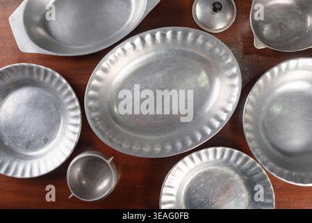 Plan au-dessus de plats de service en étain, assiettes et bols sur une table en bois sombre. La lumière douce du studio met en valeur les textures. Convient pour vintage, décoration à la maison, Banque D'Images