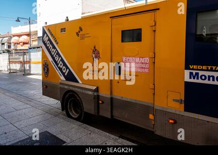 Une camionnette de sécurité blindée jaune Mondialpol stationnée dans une rue pavée d'Olbia, en Sardaigne, arborant des logos et des panneaux d'avertissement italiens. Banque D'Images
