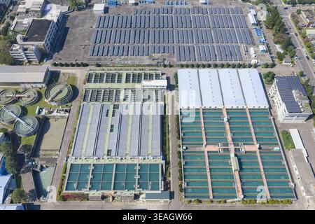 Vue aérienne d'une grande usine de traitement de l'eau avec des réservoirs de filtration rectangulaires, des clarificateurs circulaires et de vastes panneaux solaires sur le toit Banque D'Images