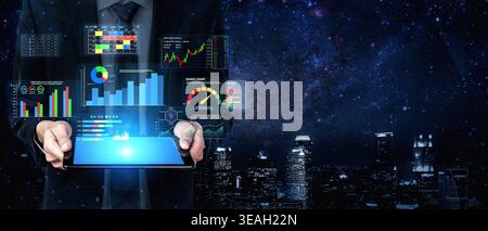 Homme d'affaires tenant une tablette numérique affichant des analyses futuristes et des graphiques tout en se tenant contre l'horizon de la ville sous un ciel étoilé de nuit Quark. Banque D'Images