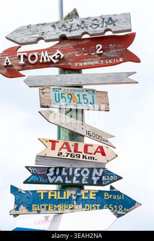Panneau de signalisation directionnel éclectique empilé avec des flèches en bois colorées et altérées pointant vers des endroits éloignés Banque D'Images