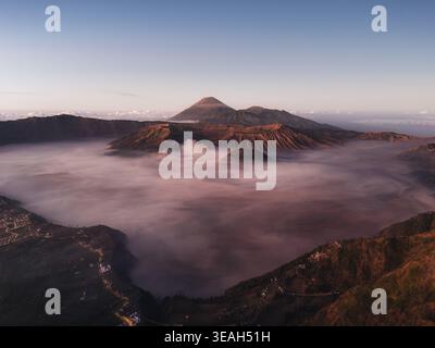 Vue aérienne des sommets volcaniques du parc national bromo Tengger Semeru s'élevant au-dessus d'une épaisse mer de brume au lever du soleil bromo, Java oriental, Indonésie. Banque D'Images