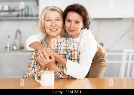 Dans la cuisine, fille et une mère mature embrassant et buvant du thé Banque D'Images