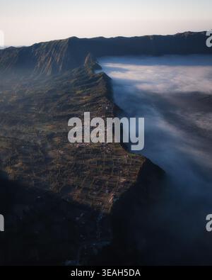 Vue aérienne du parc national bromo Tengger Semeru avec un village de crête de montagne et un épais brouillard remplissant la caldeira pendant le lever du soleil bromo, East Java, Ind Banque D'Images