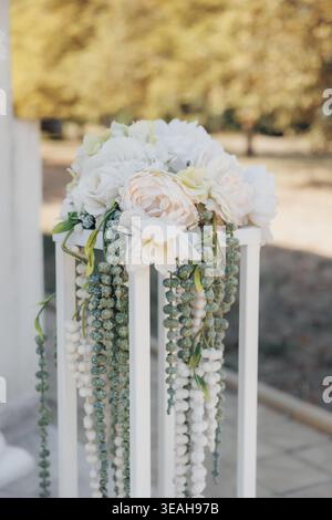 Cascade de roses blanches sur un grand stand avec verdure traînante et perles, toile de fond de passerelle extérieure créant une atmosphère romantique douce Roses crème, eucalyptus Banque D'Images