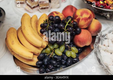 Affichage coloré de fruits pour la célébration. Mélange vibrant de bananes, raisins et pêches pour servir. Arrangement de bananes mûres raisins et pêches création Banque D'Images