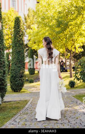 Mariée élégante sur Garden Path. Mariée contemporaine avec cheveux tressés dans un cadre serein. Figurine de mariée sophistiquée navigant parfaitement entretenue Banque D'Images