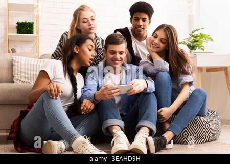 Groupe d'amis qui passent du temps ensemble tout en regardant du contenu sur un appareil mobile à l'intérieur Banque D'Images