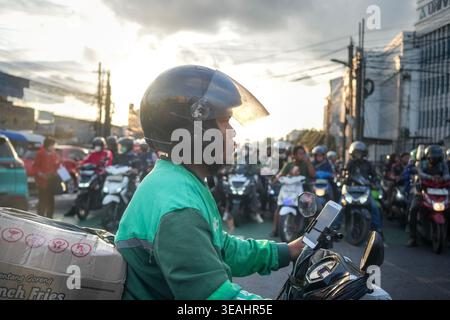 Jakarta, Indonésie - 2 février 2026 - profil latéral d'un livreur sur une moto transportant un colis, naviguant à travers de lourdes heures de pointe tra Banque D'Images