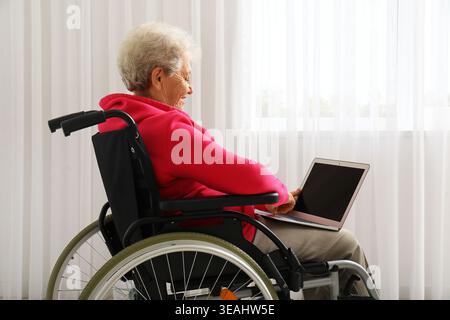 Femme âgée en fauteuil roulant utilisant un ordinateur portable à la maison Banque D'Images