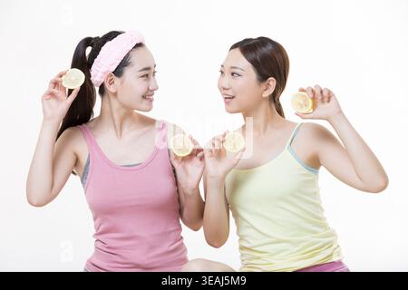 Deux jeunes femmes, une avec un bandeau rose, tenant des tranches de citron et souriant l'une à l'autre. Banque D'Images