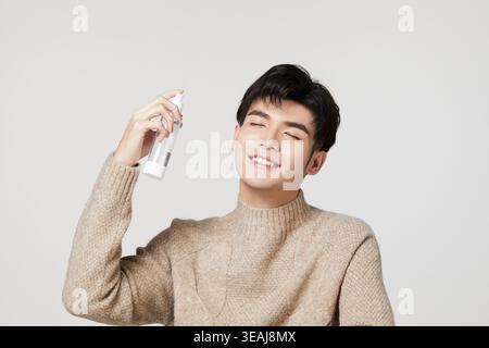 Un jeune homme asiatique dans un pull tient une bombe aérosol, souriant les yeux fermés. Banque D'Images