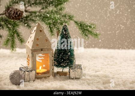 Un petit arbre de Noël, une lanterne blanche avec une bougie allumée et des boîtes-cadeaux sont placés sur un sol enneigé. Banque D'Images