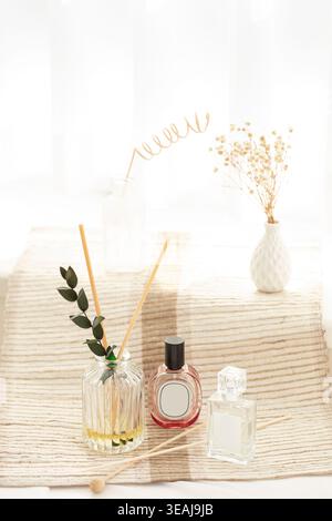 Une sélection de flacons de parfum et un diffuseur de roseau reposent sur une nappe de couleur crème, entourés de fleurs délicates et d'une sculpture en fil d'or. Banque D'Images