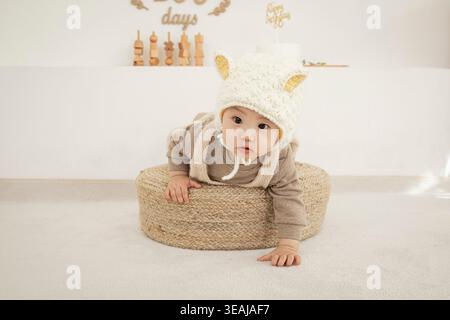 Un bébé dans un chapeau de mouton blanc se trouve sur un panier tissé, regardant curieusement la caméra. Banque D'Images