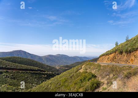 Une route sinueuse traverse un paysage de montagne verdoyant sous un ciel bleu clair. Banque D'Images