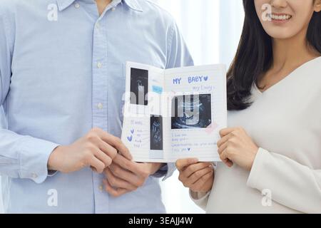 Un couple tient un livre d'échographie pour bébé, souriant et célébrant leur bébé à venir. Banque D'Images