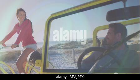 Couple souriant appuyé sur des véhicules jaunes sur des dunes, femme portant un dessus rose, volant visible Banque D'Images