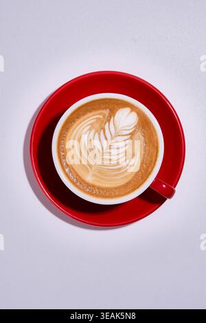 Tasse rouge contient un café lisse avec de la mousse. Boisson chaude servie dans une tasse rouge vif sur une surface blanche Banque D'Images
