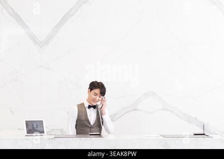 Une jeune réceptionniste asiatique répond à un appel téléphonique dans un hall d'hôtel moderne. Banque D'Images