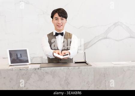Une réceptionniste de l'hôtel remet une carte-clé à un client à la réception. Banque D'Images