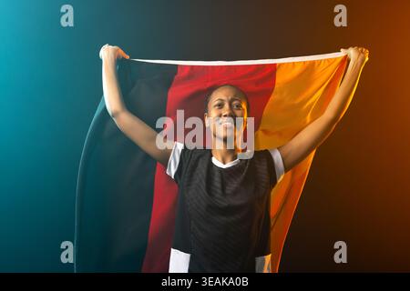 Femme afro-américaine portant une chemise de sport noire tenant le drapeau tricolore au-dessus de la tête dans l'éclairage de studio. Bannière, athlète, jante, sarcelle, orange, toile de fond Banque D'Images