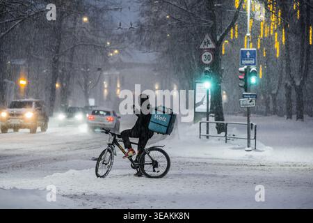 Tallinn, Estonie - 03 janvier 2025 : vue d'un cycliste bravant les fortes chutes de neige près d'un feu de circulation, avec des voitures naviguant sur les routes glissantes sous le Banque D'Images